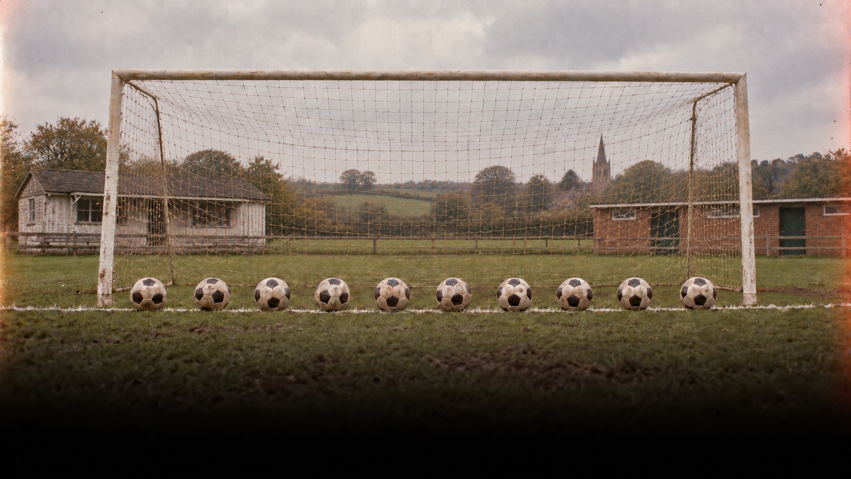 Ten training footballs lined up in front of a village football goal